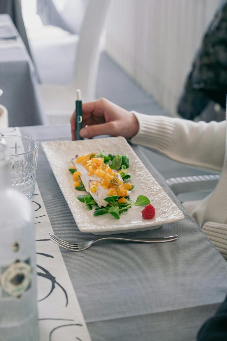 Elegant seafood dish with greens and raspberry garnish in Italian restaurant setting.